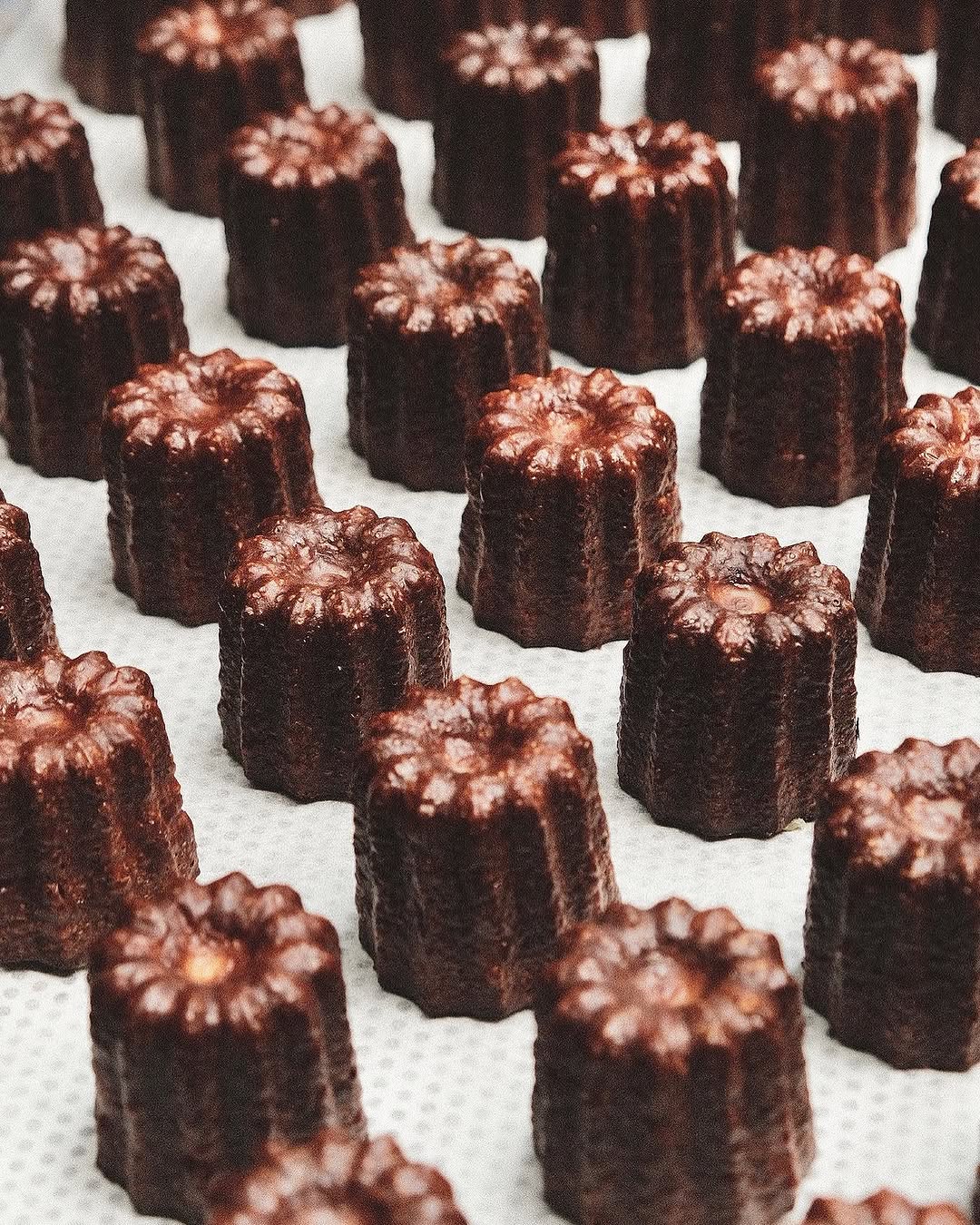 Rows of deeply caramelised canelé on baking paper