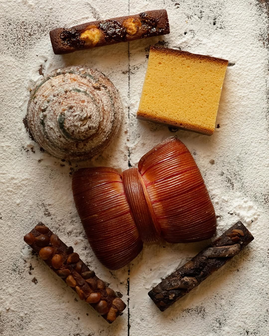 An overhead spread of financiers, castella and laminated pastries dusted with sugar