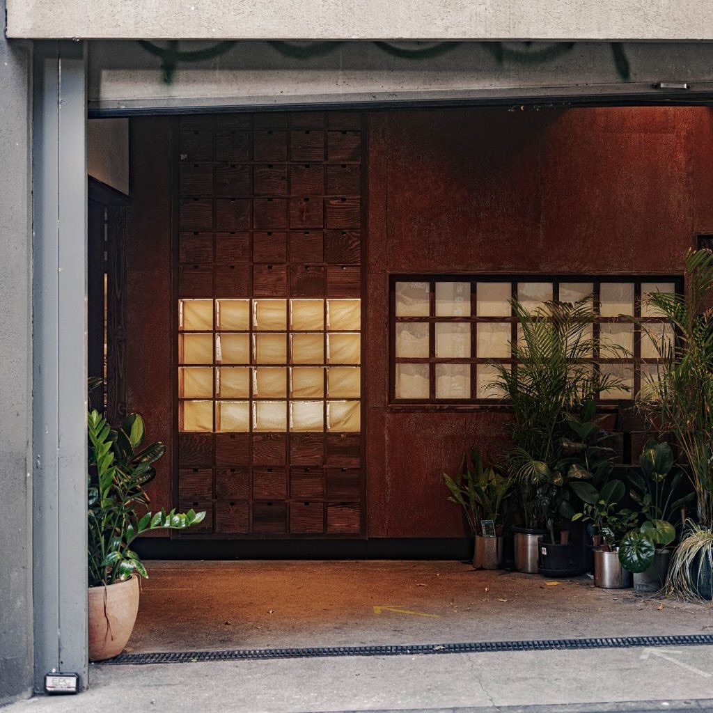 The Bakemono shopfront at dusk — Corten steel and dark timber, a backlit panel glowing within